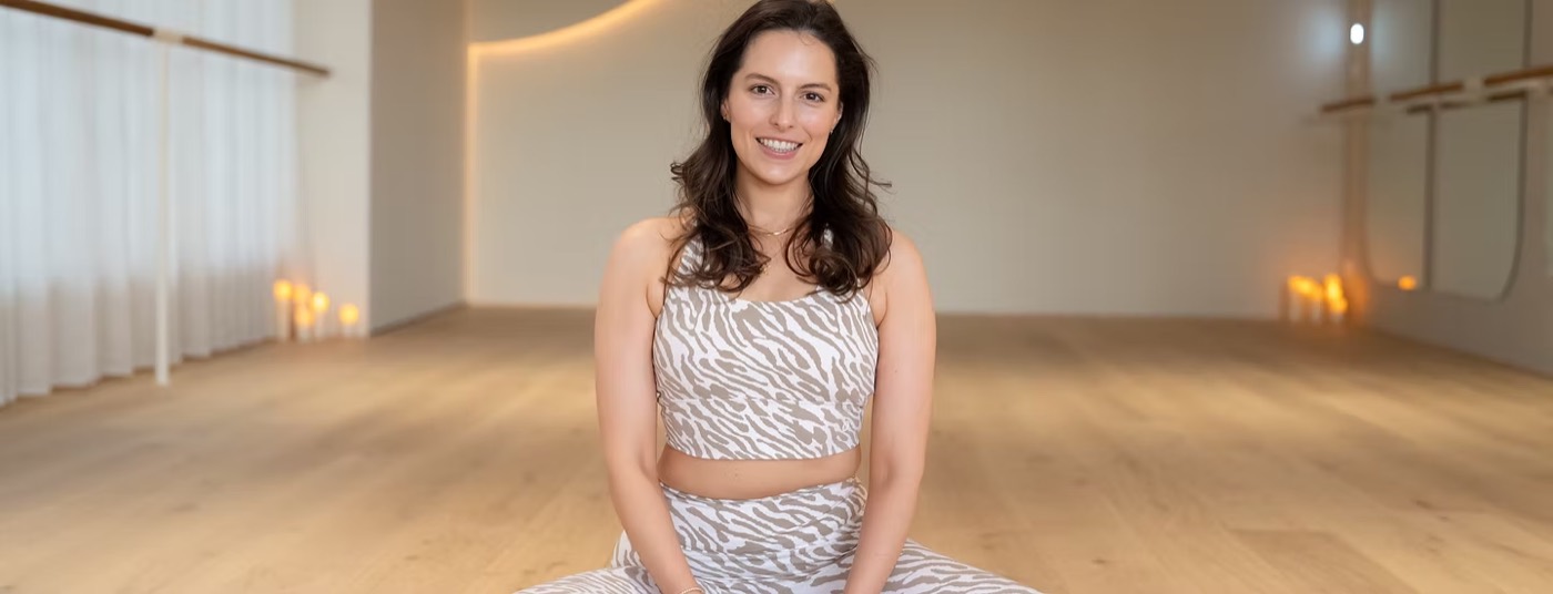 Kelsey Hopper seated on the floor of a bright yoga studio, candles along the wall behind her
